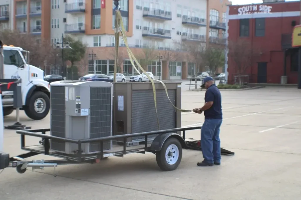 A man securing an air conditioning unit on a trailer in an urban setting.